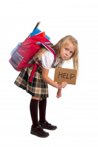 sweet little blonde schoolgirl asking for help carrying heavy backpack or school bag full causing stress and pain on back due to overweight isolated on white background